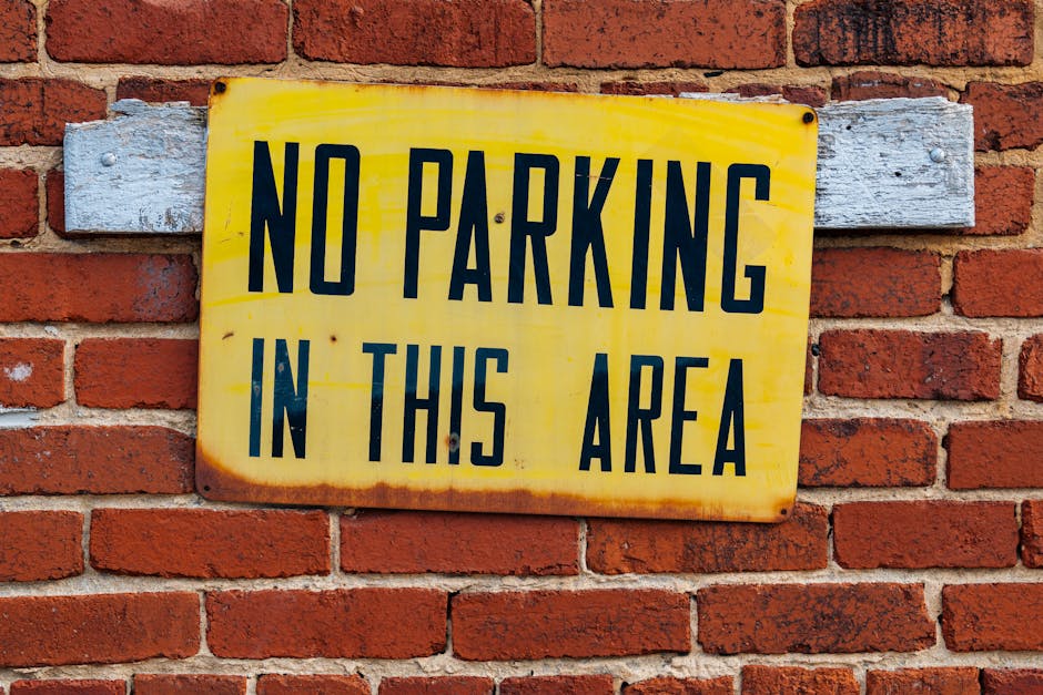 A foggy outdoor parking area with two red and black plastic barriers connected by a red ribbon that reads 'Authorised Access Only.' The barriers are positioned on a paved section with grey interlockin